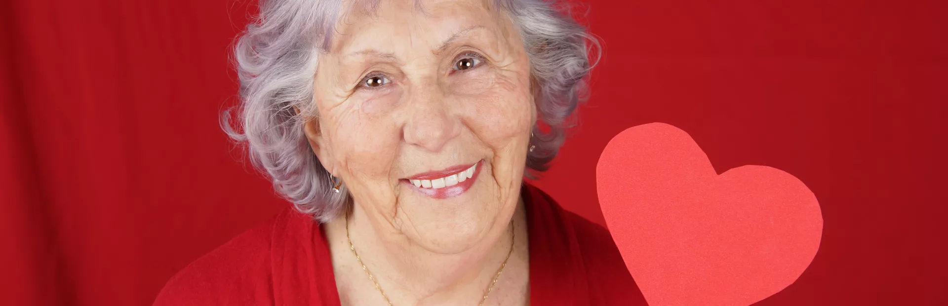 Mujer mayor sujetando un corazón de papel con fondo rojo