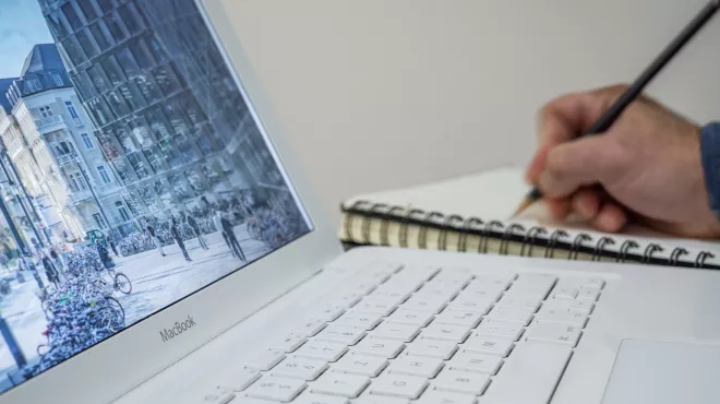 persona escribiendo con un lápiz en un cuaderno frente a la pantalla de su ordenador